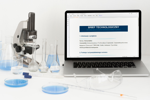 Laptop z wyświetlonym dokumentem „Brief technologiczny”. Obok sprzęt laboratoryjny: mikroskop, zleweki z błękitnym płynem i okulary ochronne.
