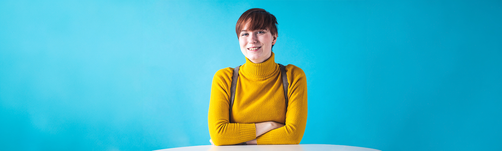 Kuvassa nainen hymyilee kameralle turkoosin taustan edessä.