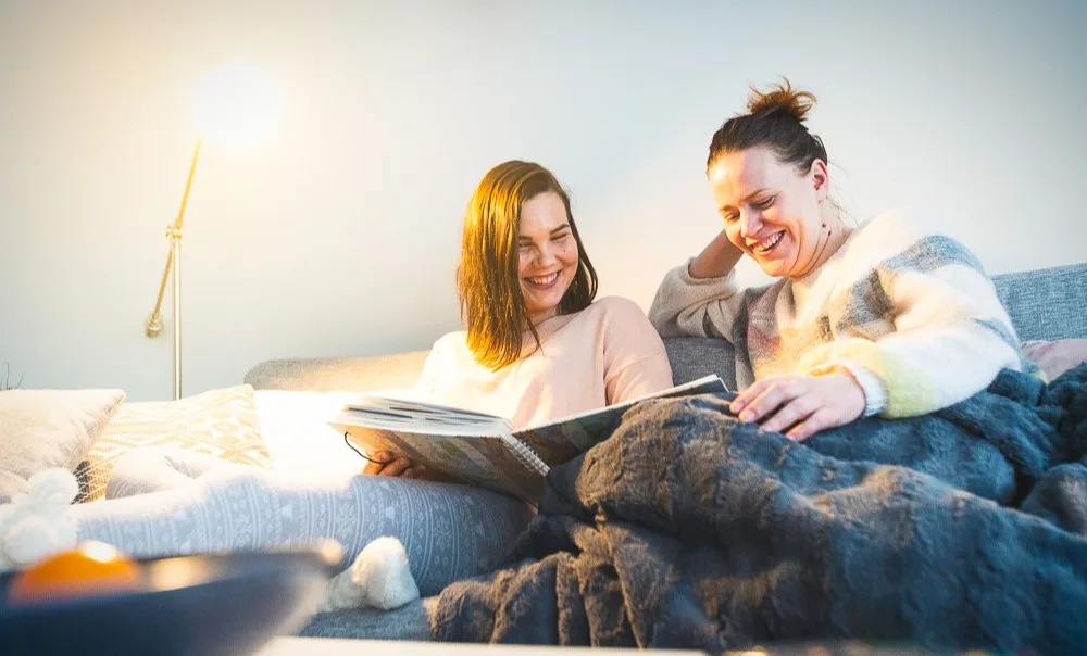 Kaksi naista istuvat sohvalla ja lukevat PKS:n kirjaa.