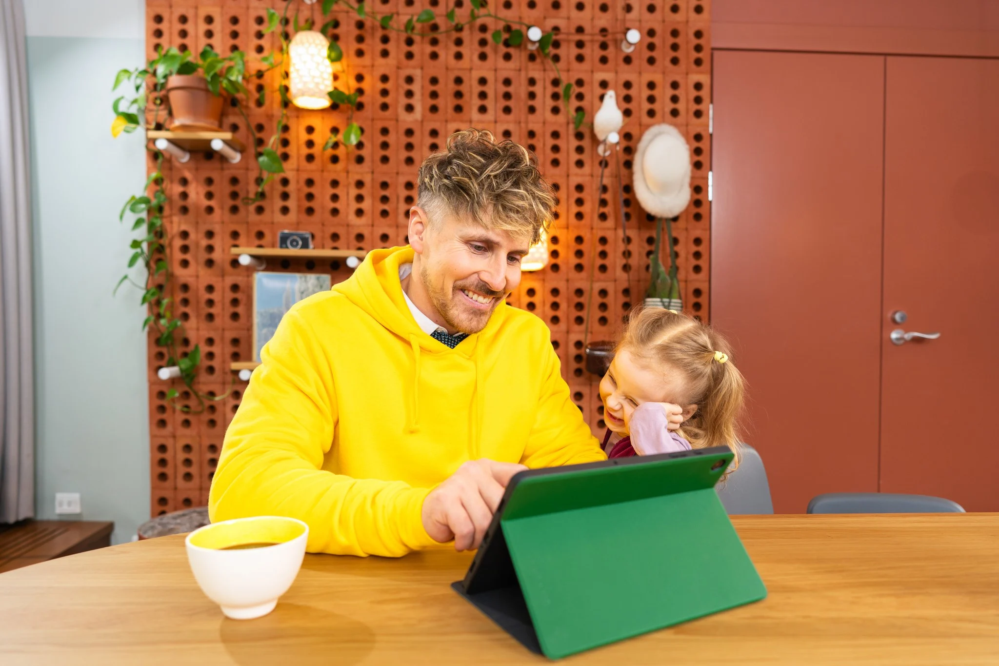 Isä ja tytär pöydän ääressä. Isä tekee töitä tabletilla.