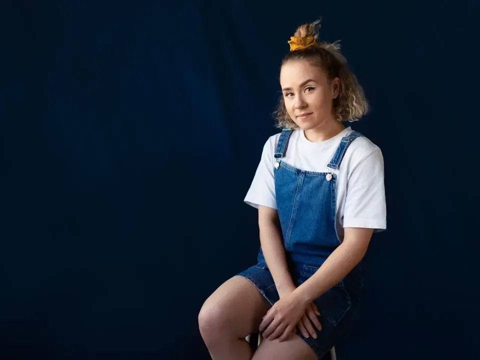 Nainen istuu tuolilla farkkuhaalari päällään