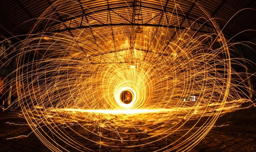 Tummaa taustaa vasten oransseja ja keltaisia kiemuroita ja valonsäteitä, jotka kuvaavat sähköä.