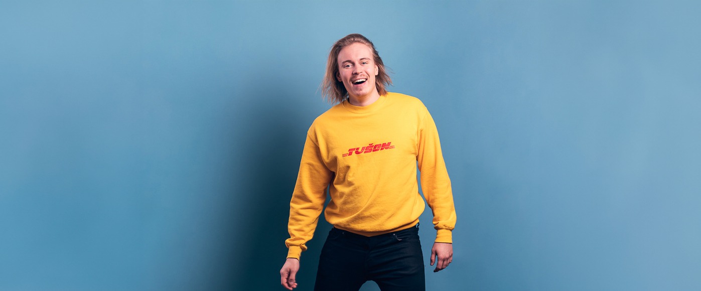 Iloinen mies on pukeutunut kirkkaaseen keltaiseen paitaan ja hymyilee katsoen kameraa.