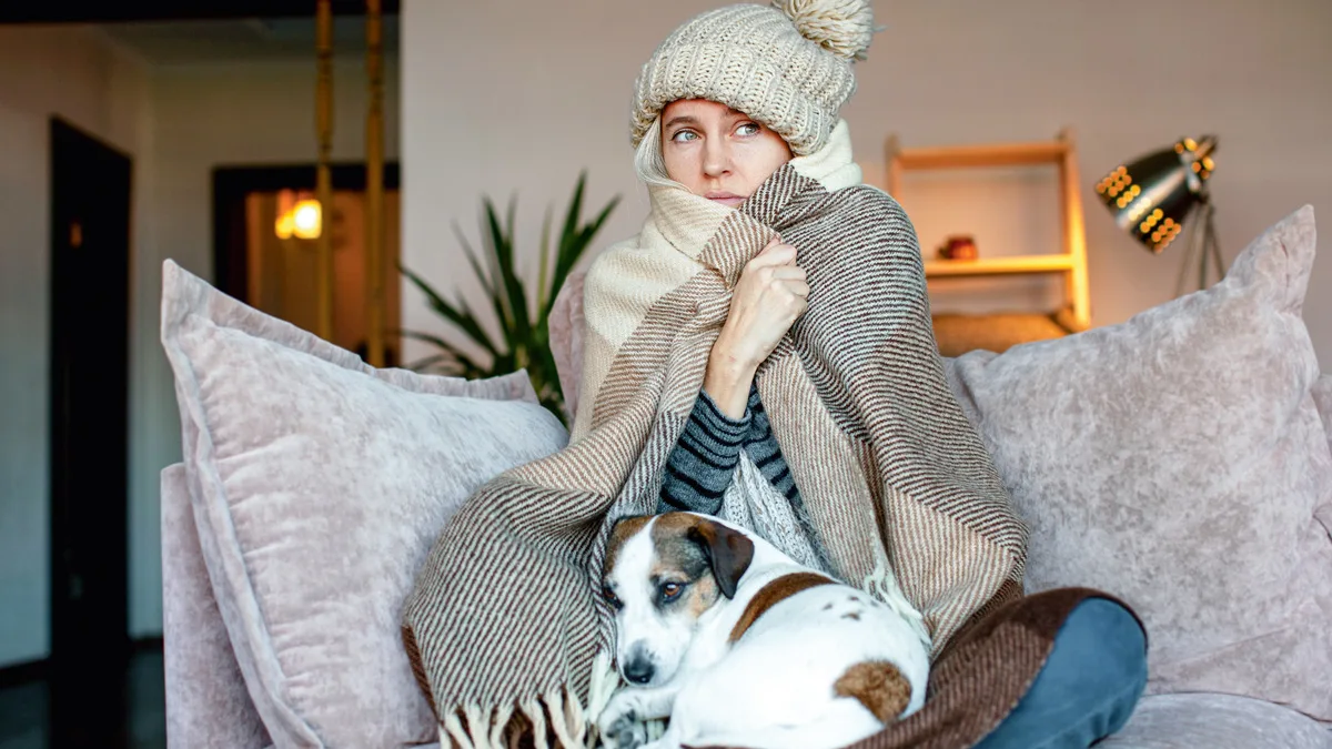 Nainen istuu kymissään sohvalla koiran kanssa.