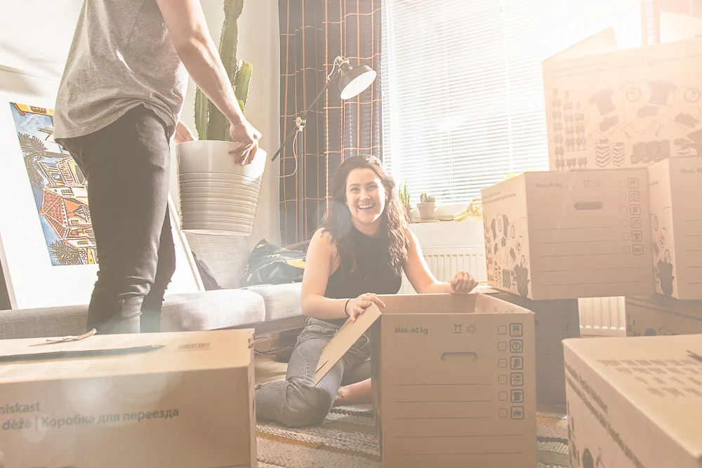 Uuteen asuntoon muuttanut nainen istuu lattialla muuttolaatikoiden ympäröimänä ja hymyilee kameralle saatuaan PKS:ltä halvan sähkösopimuksen uuteen kotiin.