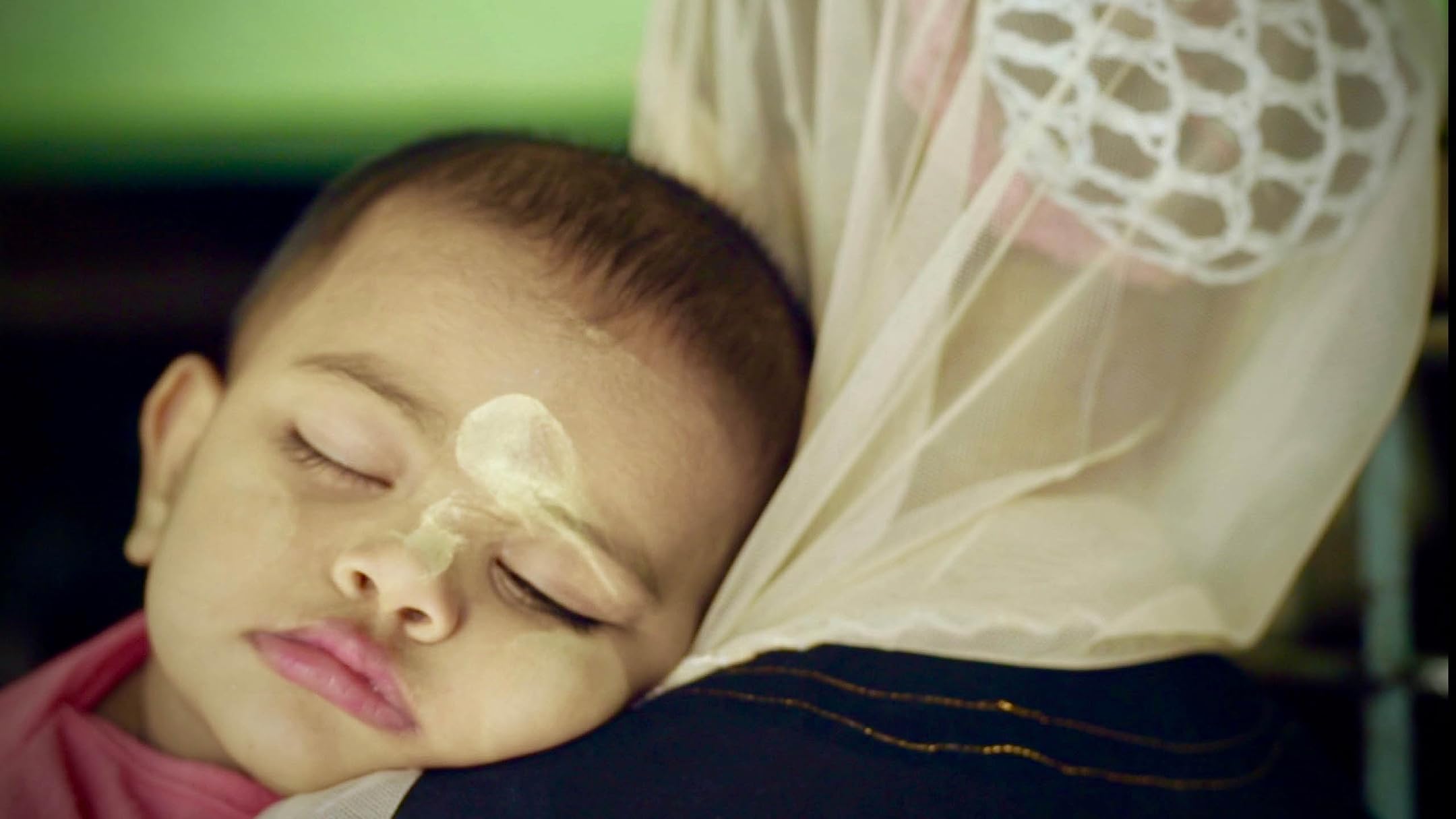 Offizielles Bildmaterial vom Film Midwives (2022). Schlafendes Kind auf dem Arm seiner Mutter.