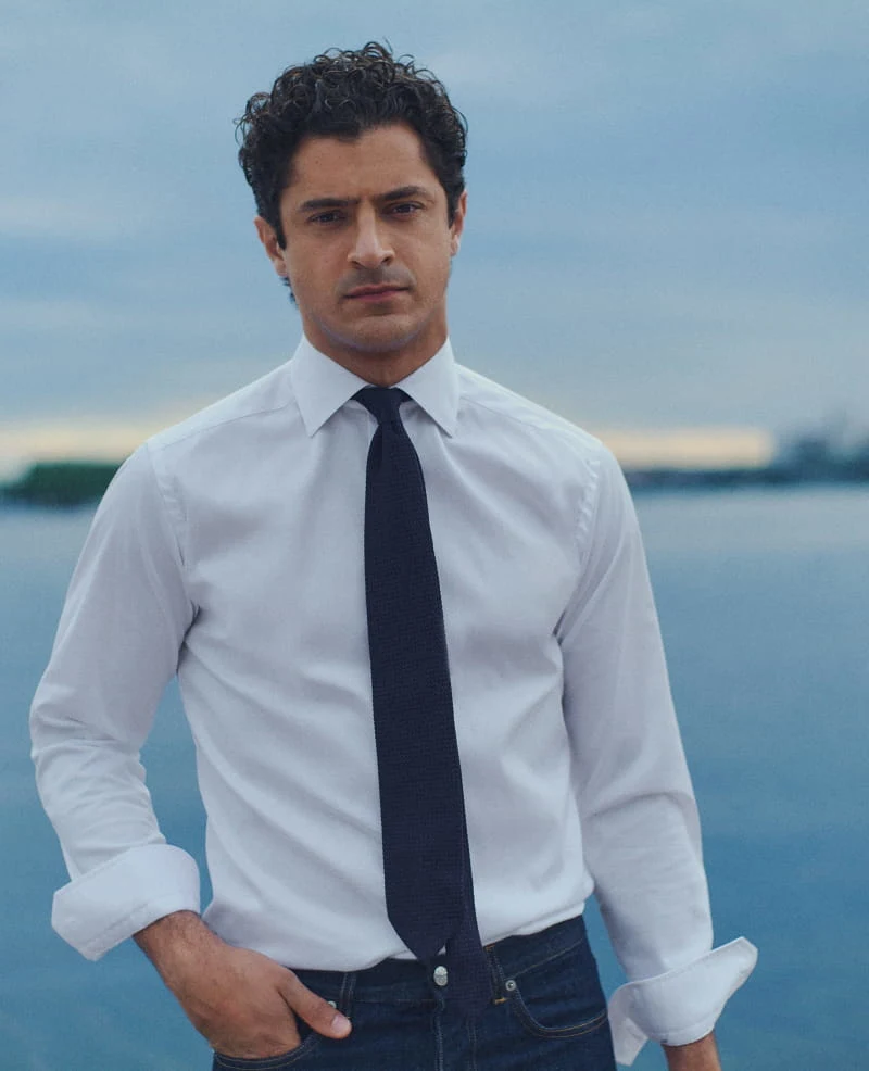 a man posing in a white signature twill shirt and a navy tie by the water