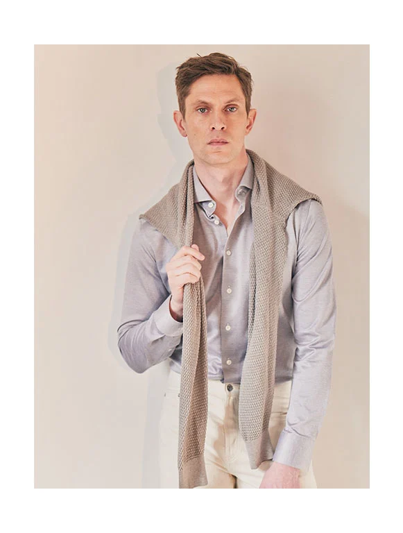 a man in a studio wearing a shirt with a sweater hanging from his shoulders posing