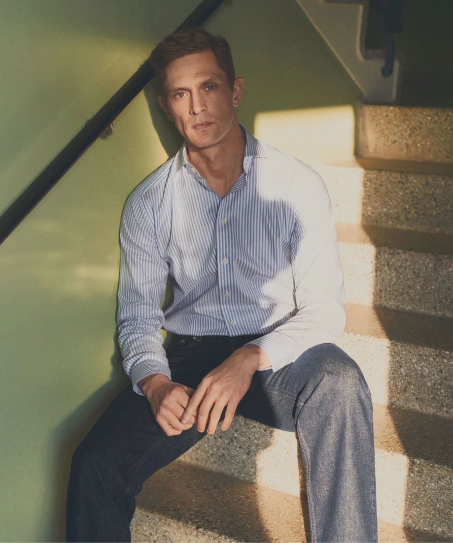 a man posing in a striped shirt by a stairwell