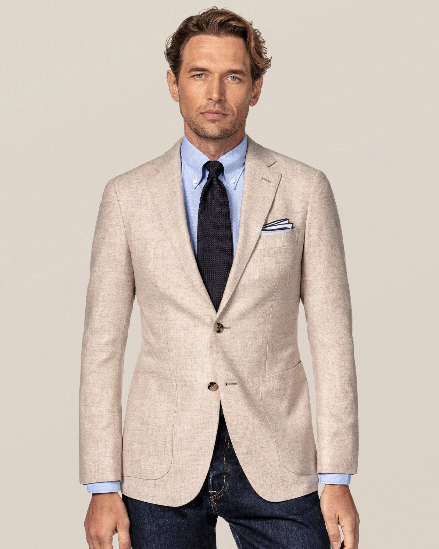 A well dressed man wearing a beige jacket, blue shirt and a matching grenadine tie