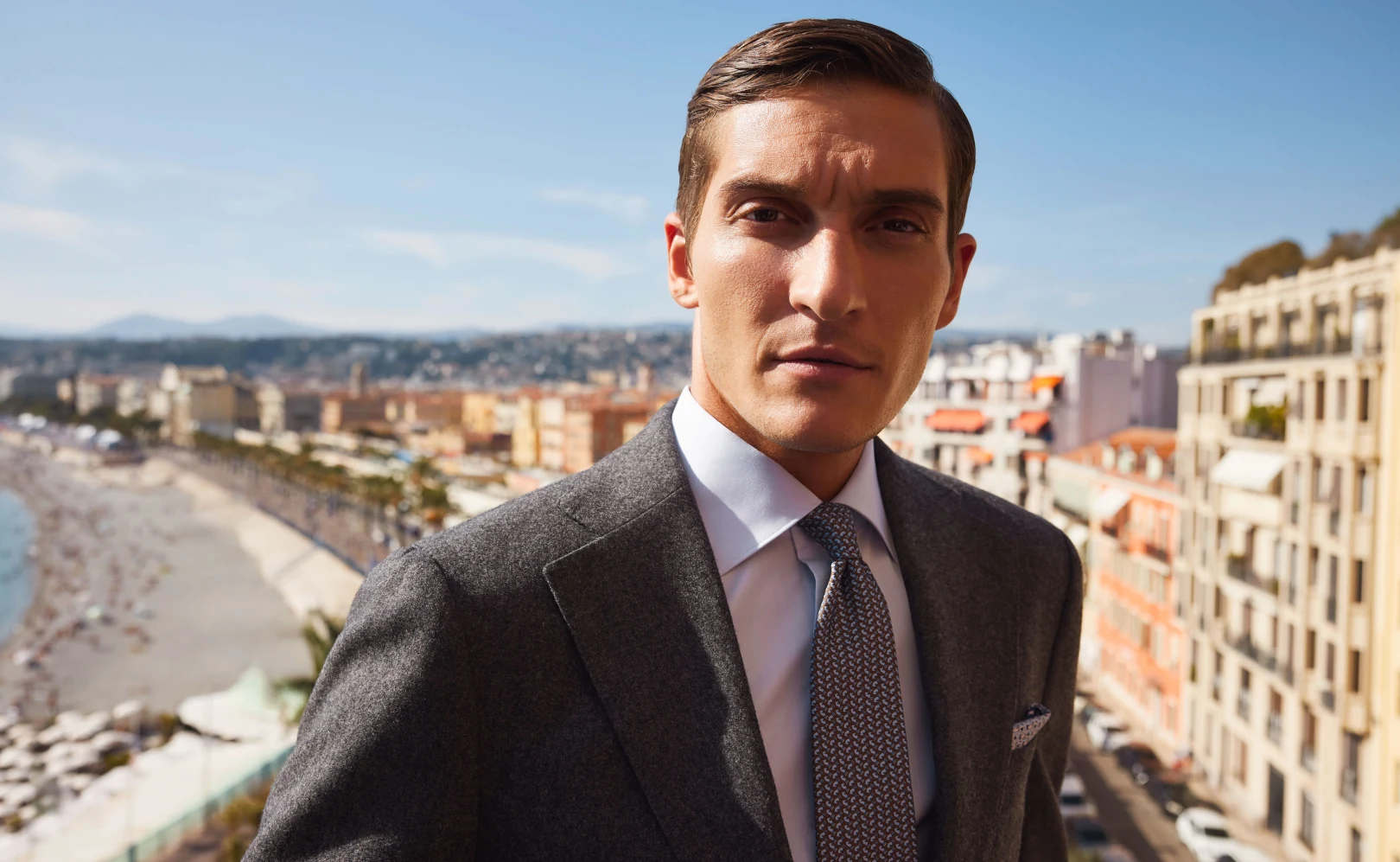 Man in a blue shirt standing on a balcony with a view over the city.