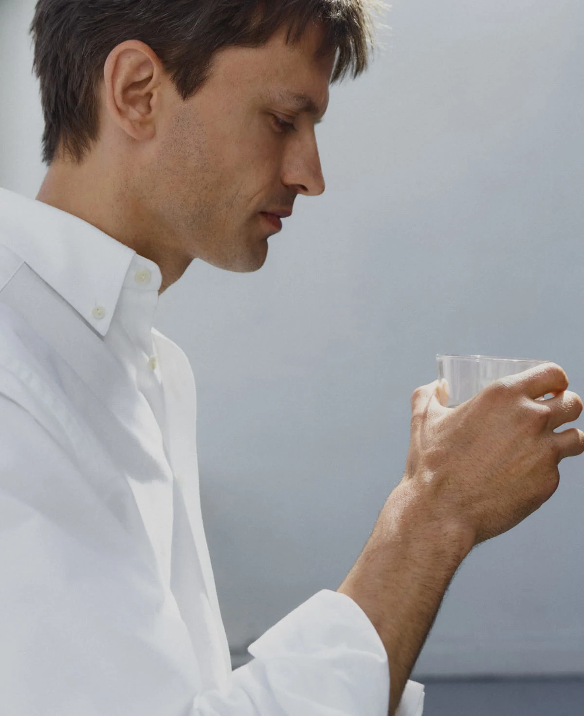 a man wearing a white eton oxford shirt drinking from a glass