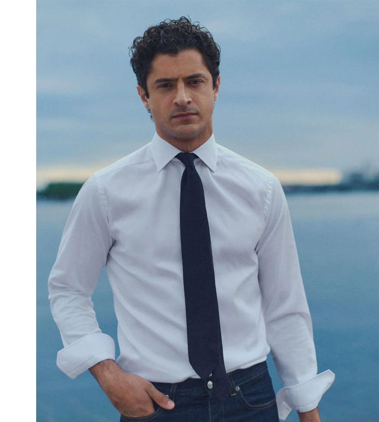 a man posing in a white signature twill shirt and a navy tie by the water