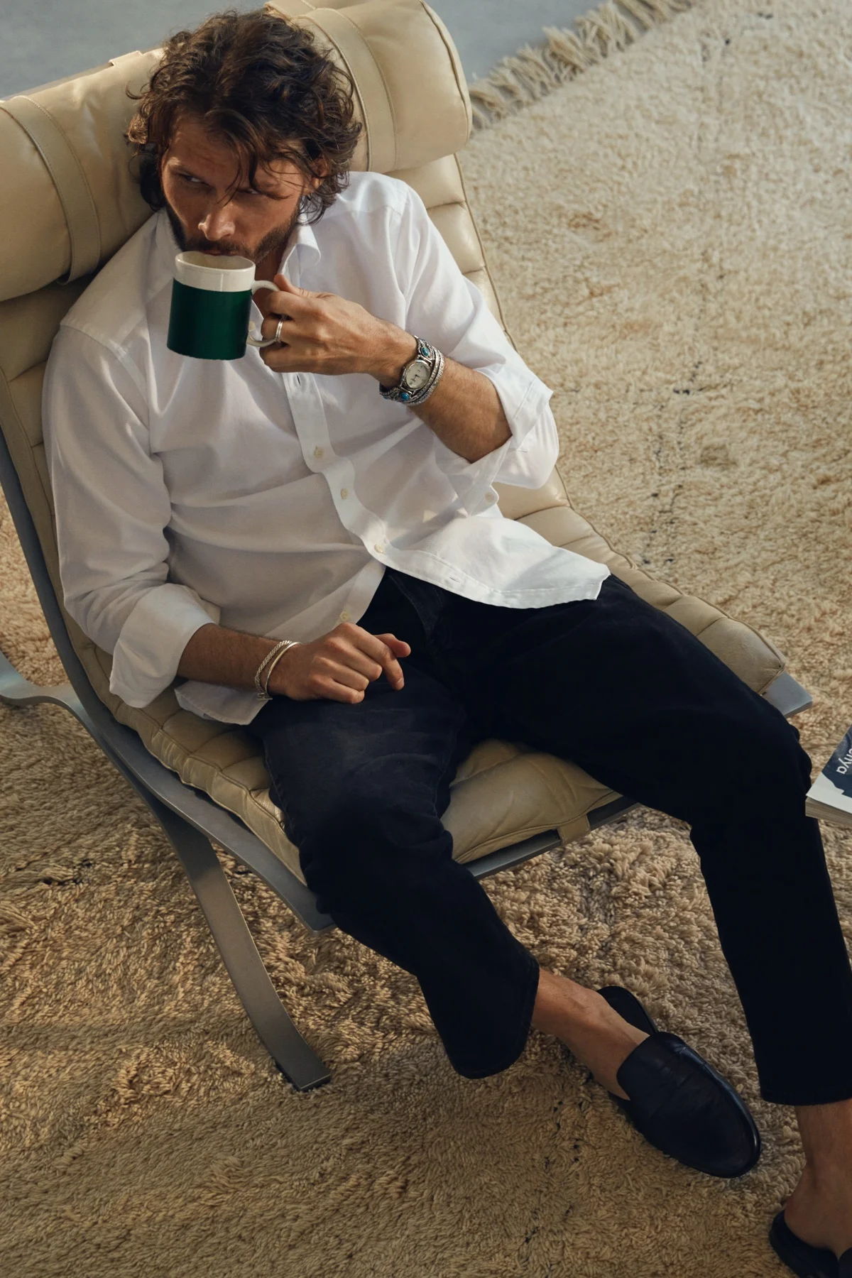 man drinking coffee in armchair wearing white shirt