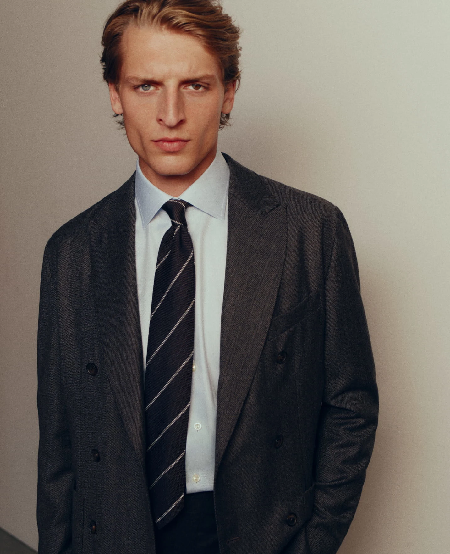 a model posing in a double breasted jacket, blue dress shirt and a tie
