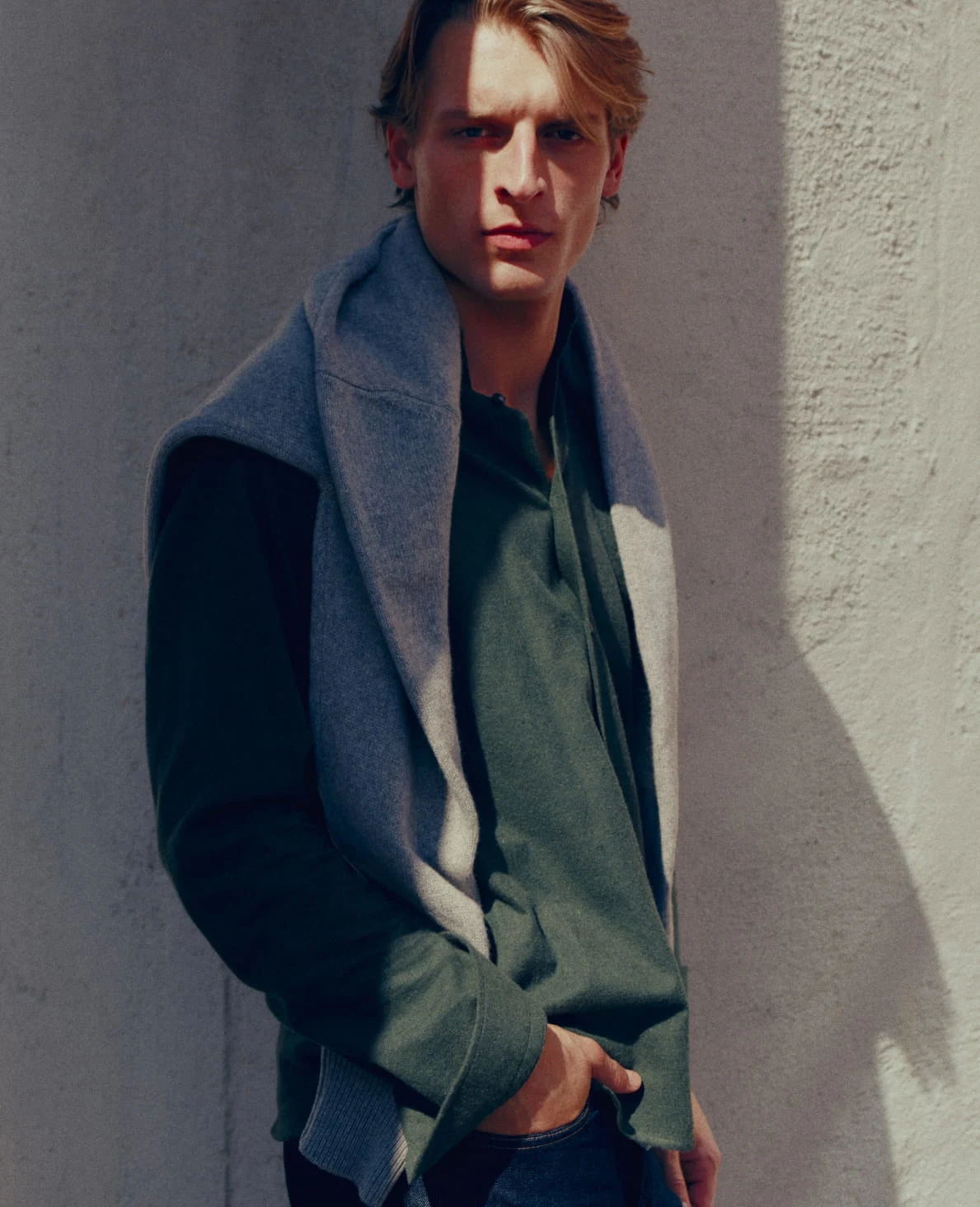 a model posing in a green flannel shirt with a cashmere sweater hanging around his neck