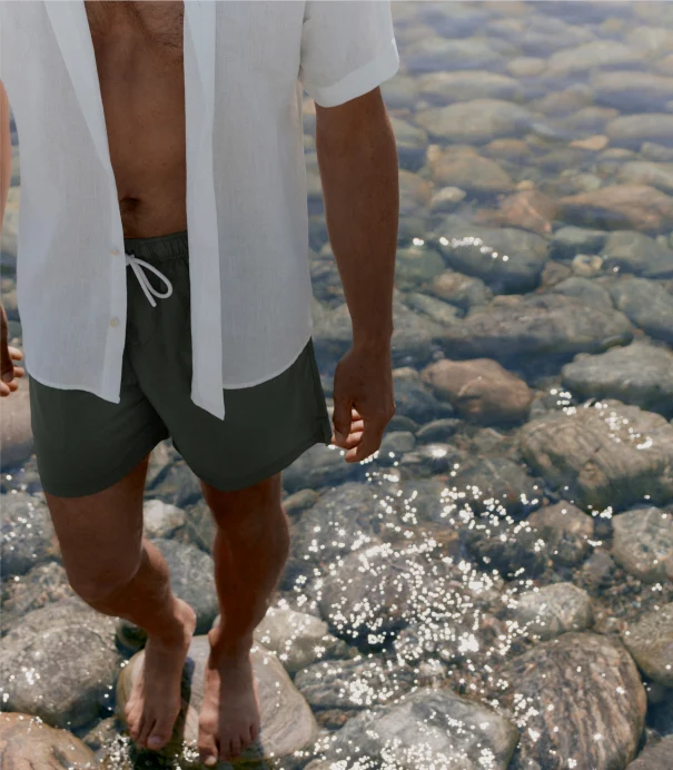 a man by the water in swim trunks and a short sleeved shirt