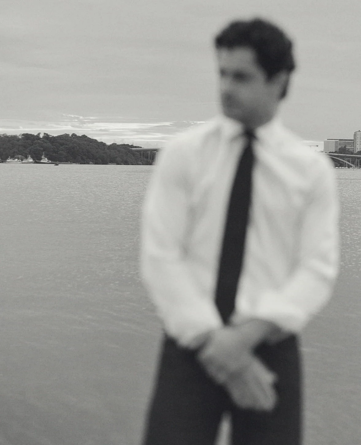 a black and white image of a man by the water wearing a crisp white signature twill shirt and a navy tie