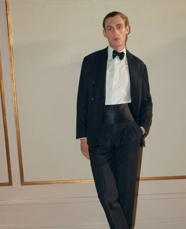 a model standing by a wall in an old room wearing a tuxedo