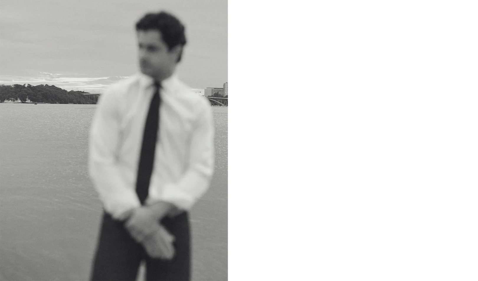 a black and white image of a man by the water wearing a crisp white signature twill shirt and a navy tie