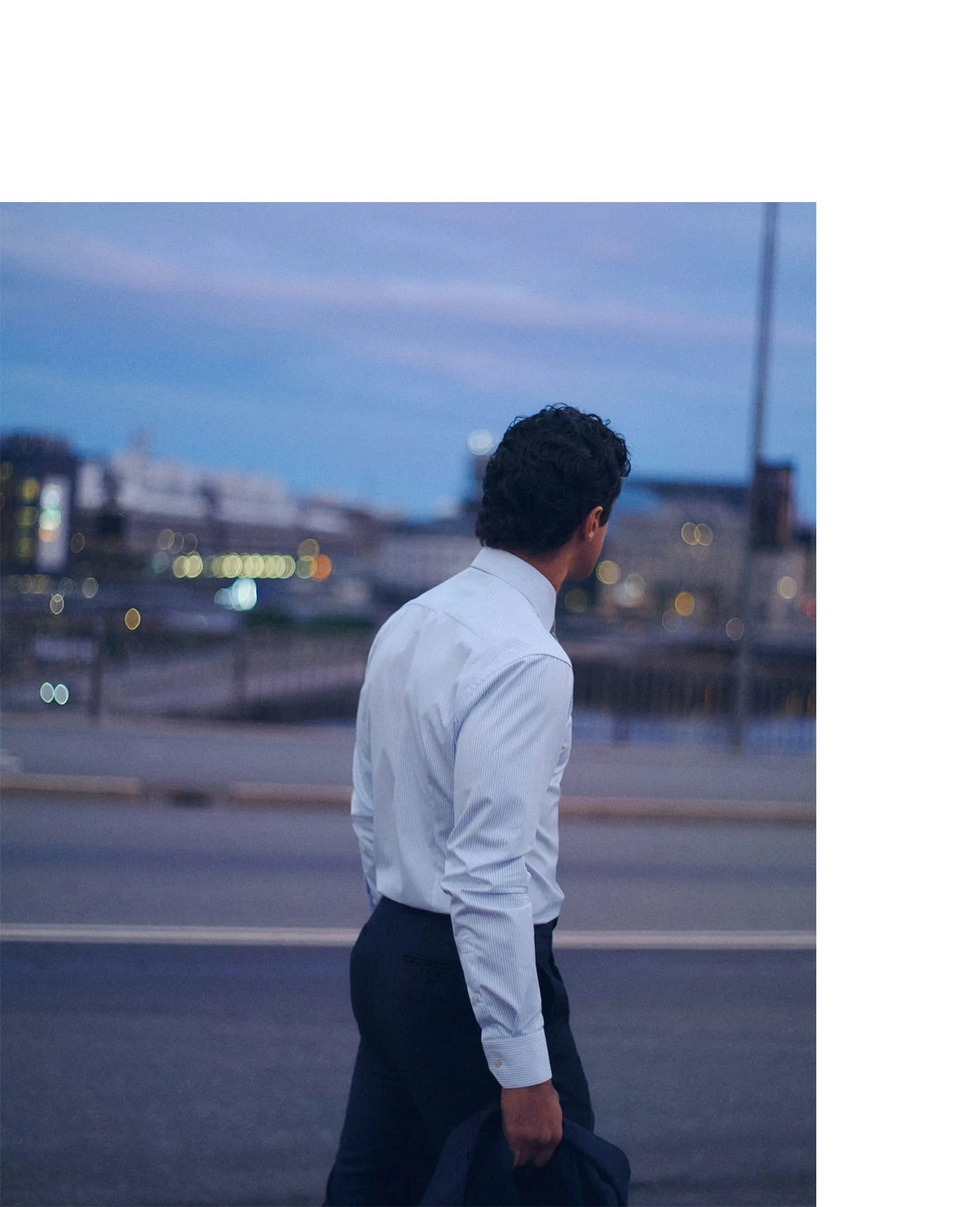 a man walking past an empty street in the evening wearing a tucked in light blue signature twill shirt