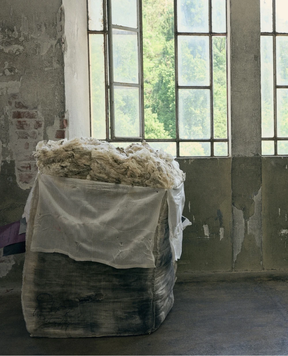 a sack full of wool and cashmere fibers put by a wall with windows in the factory