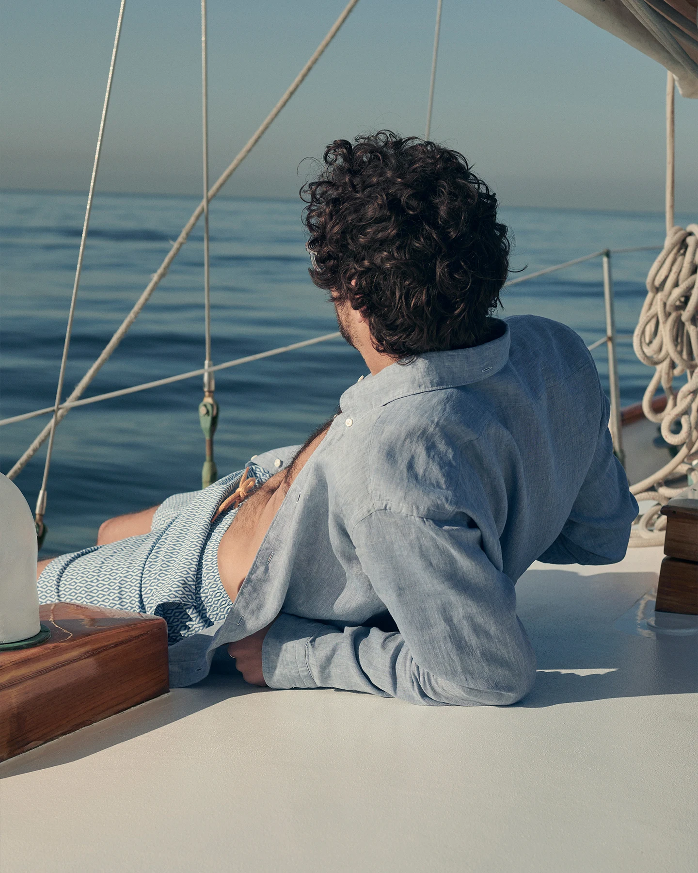 man laying on a boat, wearing a blue linen shirt