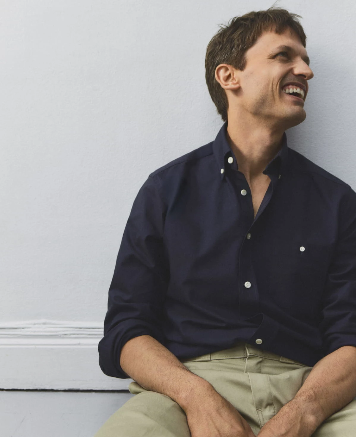 a smiling man sitting down on the floor in navy eton oxford shirt