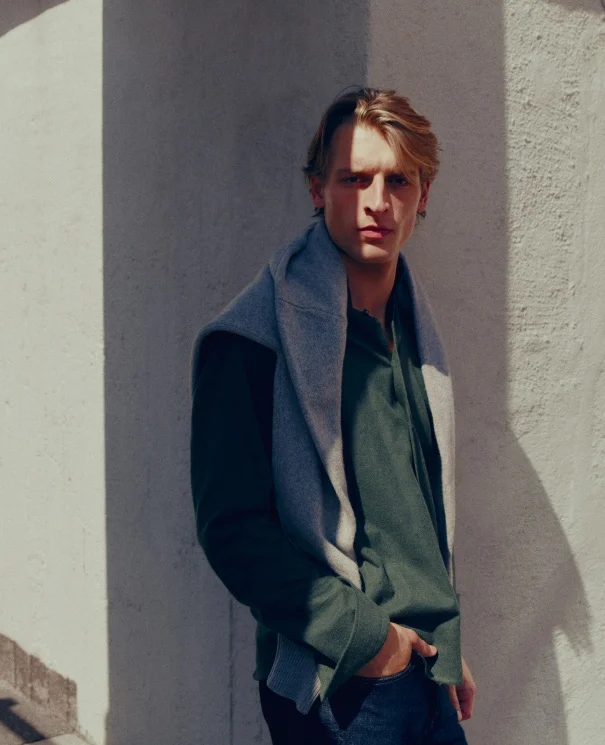 a model posing in a green flannel shirt with a cashmere sweater hanging around his neck