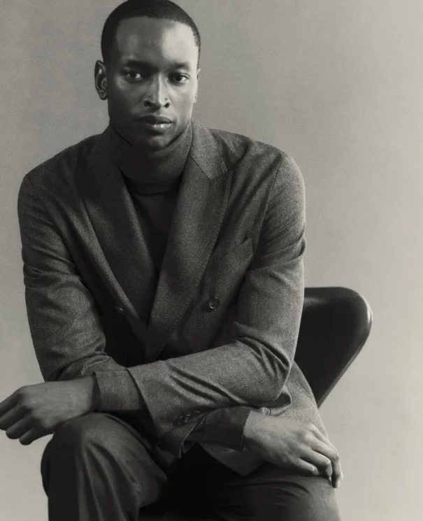 black and white shot of a model sitting posing in a turtleneck sweater and double breasted soft jacket