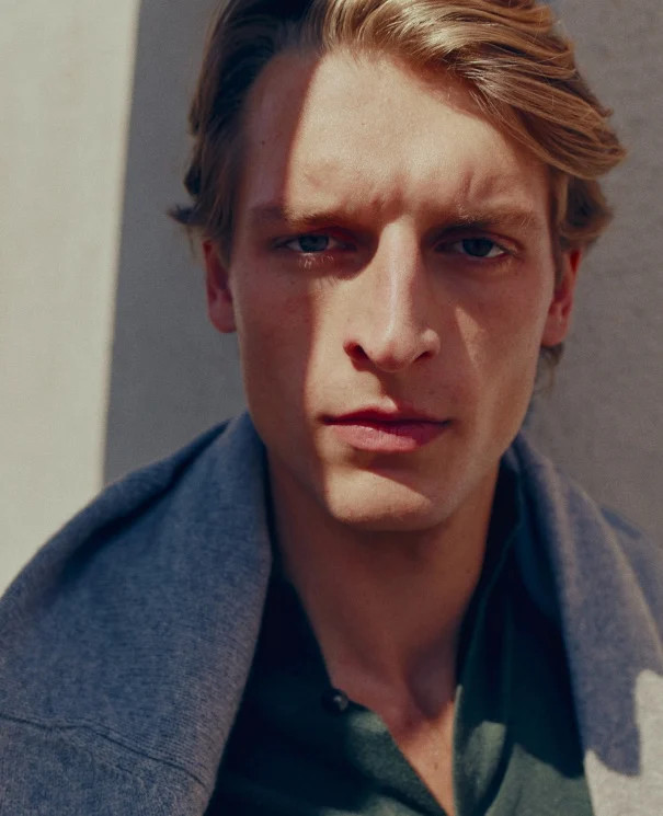 a close up shot of a model posing in a green shirt and a cashmere sweater around his neck