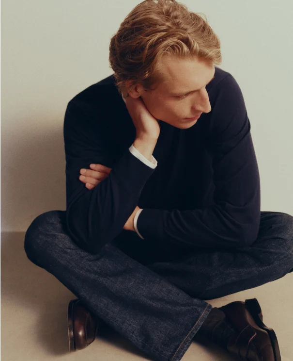 a model sitting with his legs crossed on the floor looking away