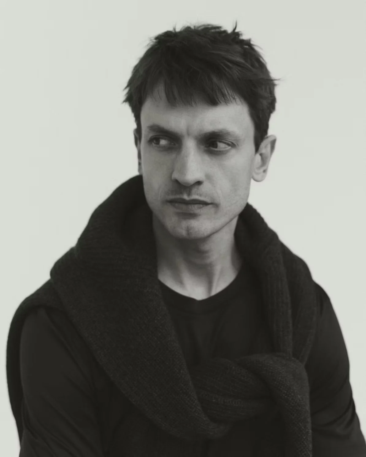 a black and white image close up image of a man wearing a navy filo di scozia t-shirt and a cashmere sweater around his shoulders