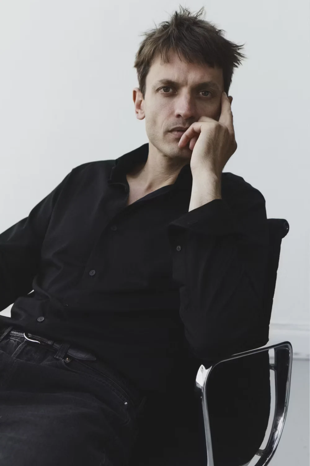 a man sitting on a chair in a studio wearing a shirt posing