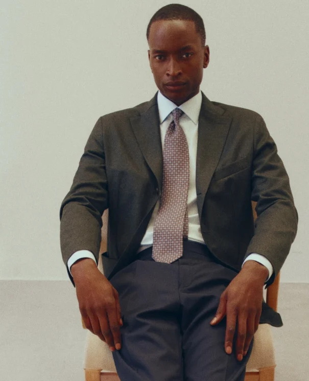 a posing model in a chair with a soft jacket, dress shirt and tie