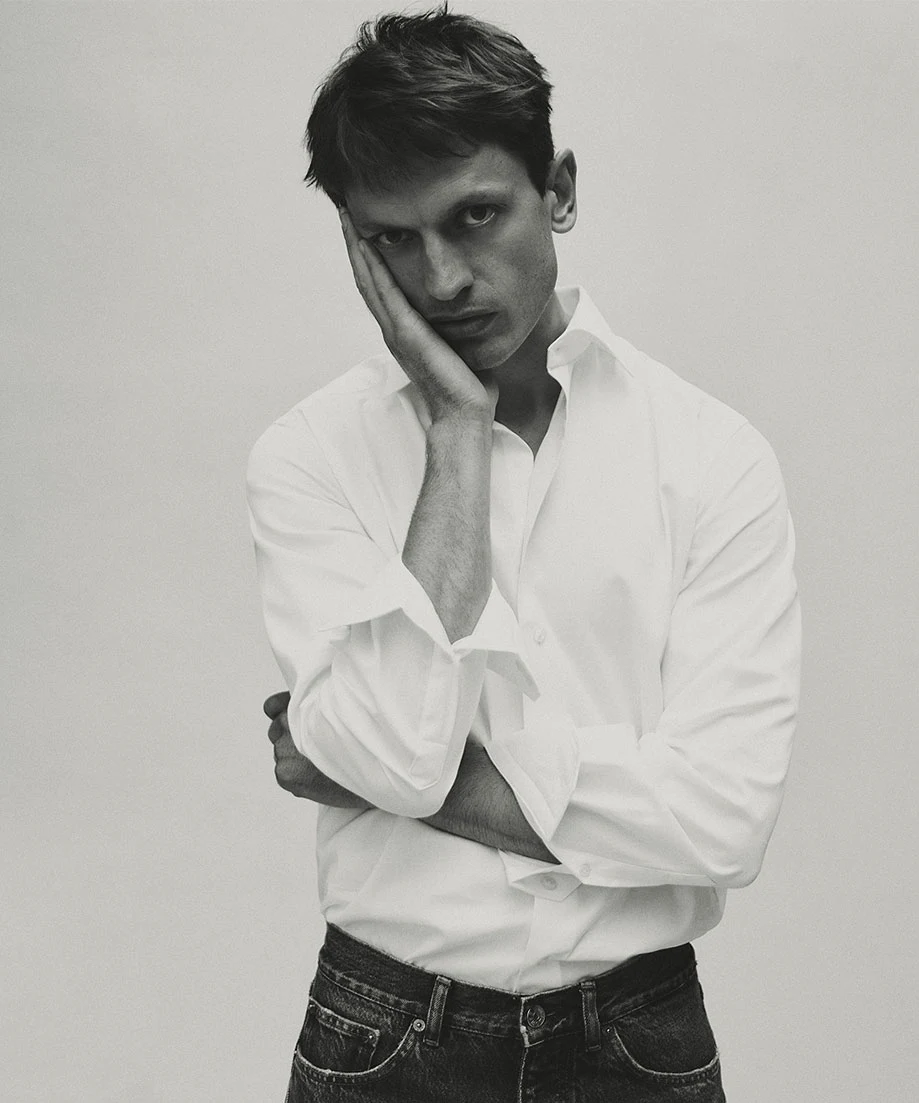 a man posing in a oxford shirt resting his head on the palm of his hand