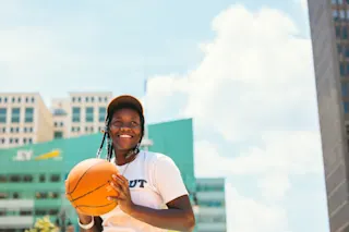 A girl holds a basketball on a sunny day. 