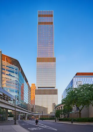 A straight-on exterior photo of the Edition tower at Hudson’s Detroit, taken from street-level, with the Detroit People Mover track in the foreground.