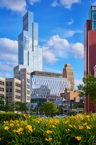 Exterior photo of Hudson’s Detroit, with a bed of yellow flowers in the foreground, and featuring the Hudson’s Block in front of the Edition.