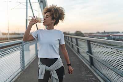 Visuel d'une femme qui boit une bouteille d'eau sur un pont