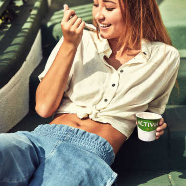 Frau isst liegend und glücklich einen Activia-Joghurt