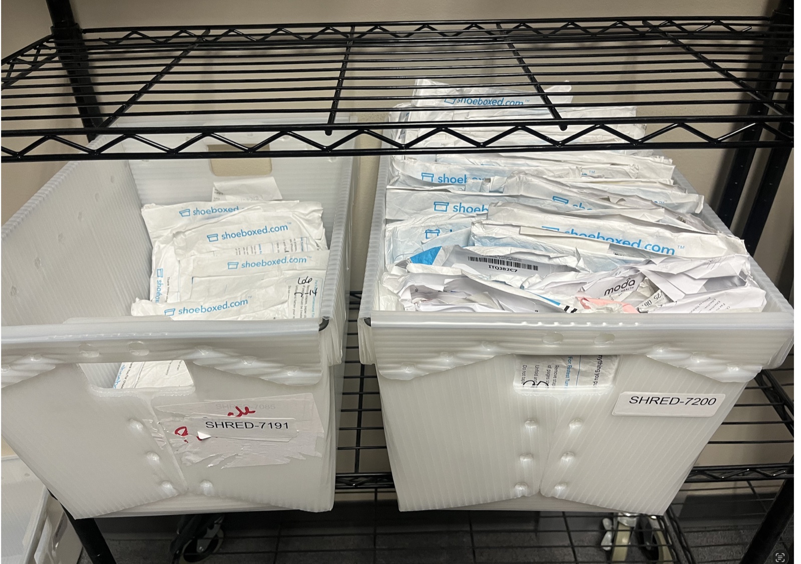 Two large white plastic bins labeled SHRED-7191 and SHRED-7200, full of processed Shoeboxed Magic Envelopes ready for secure shredding