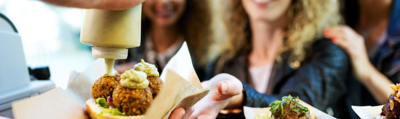 Un groupe de trois femmes se tienne devant un homme entrain de préparer un sandwich au falafels