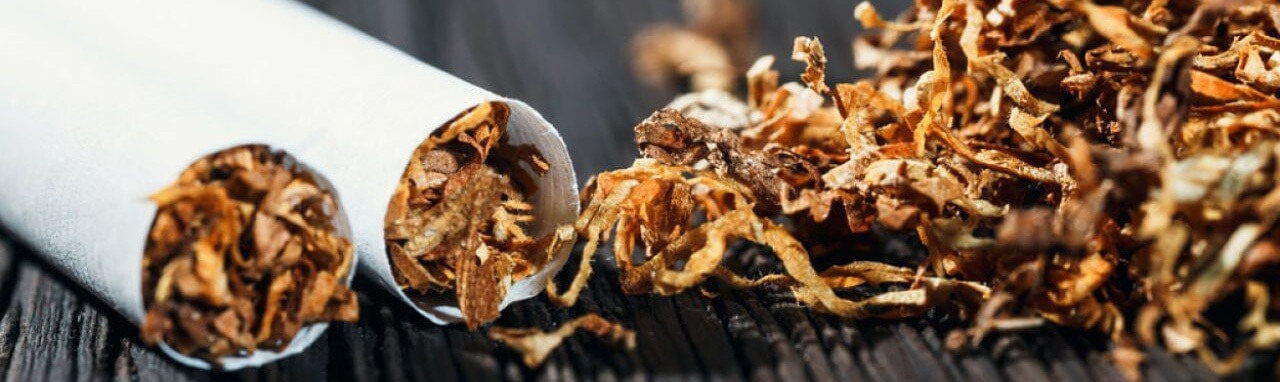 Deux cigarettes et un petit tas de tabac sur une table en bois