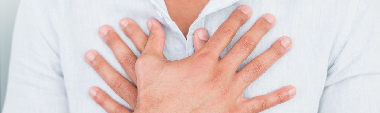 un homme en chemise claire se tient la poitrine avec les deux mains croisées.