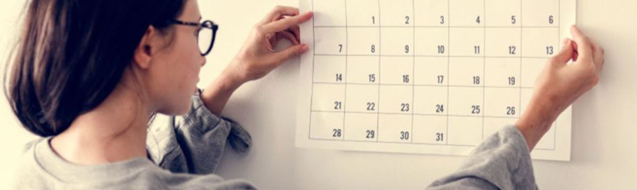 Une femme accroche un calendrier sur un mur blanc