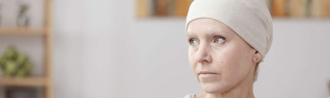 Une femme atteinte d'un cancer est assise sur un canapé, une main est posée sur son épaule comme pour la réconforter