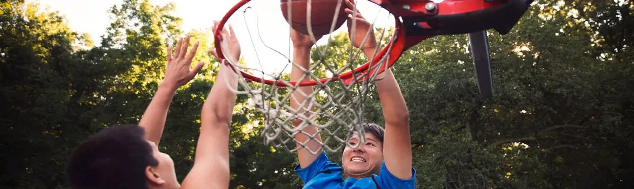 Deux hommes sautent pour attraper une balle au dessus d'un panier de basket