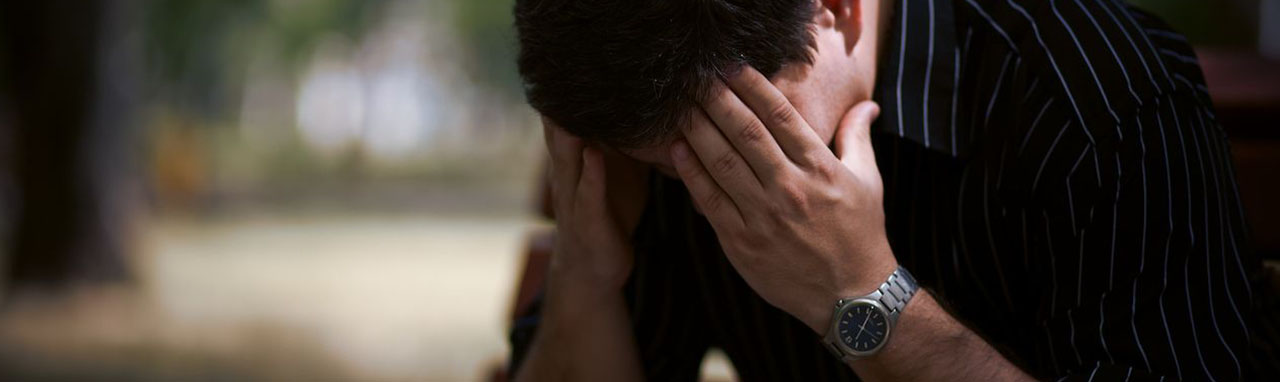 Un homme est assis dans un par cet tient sa tête entre ses mains pour montrer qu'il à des difficultés de concentration