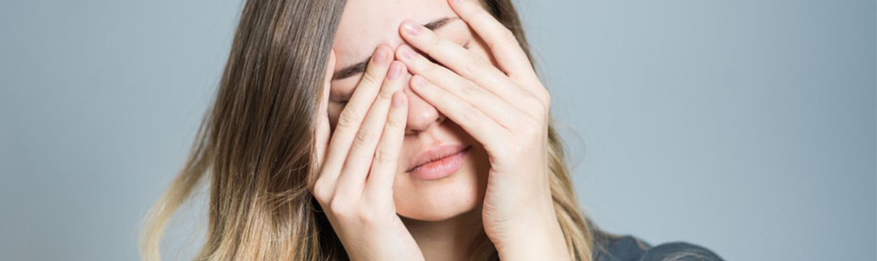 Une femme se tient la tête entre les mains sur un fond gris